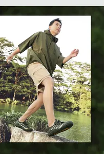 Detail of man wearing green quick-dry hiking shoes walking on rocks near a lake