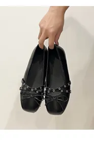 Detailed macro shot of black ballet flats featuring elegant bow and grommeted cross straps