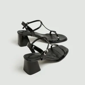 Detailopname van zwarte laklederen sandalen met blokhak en een elegant T-band ontwerp.