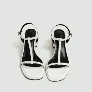 Gedetailleerd overzicht van witte T-strap sandalen met blokhak en zwarte binnenzool