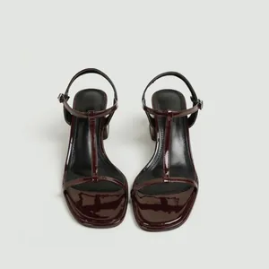 Detail van bordeauxrode laksandalen met T-bandje, blokhak en een vierkante neus.