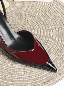 Detailaufnahme der glänzenden burgunderroten und schwarzen Lackleder-Spitze eines High Heels.