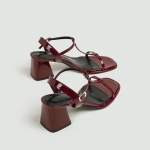 Detailopname van elegante bordeauxrode laksandalen met blokhak en een enkelbandje.