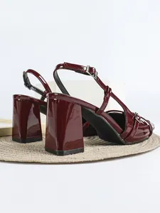 Primo piano di eleganti sandali in vernice bordeaux con tacco largo e cinturino.