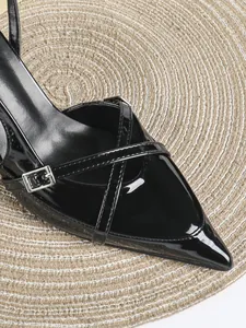 Dettaglio di décolleté in vernice nera con cinturini incrociati e fibbia alla moda