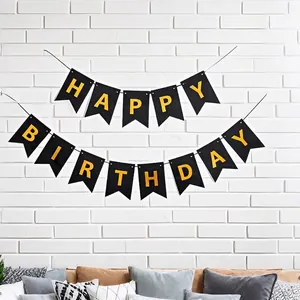 Black and gold Happy Birthday swallowtail banner hanging on a white brick wall