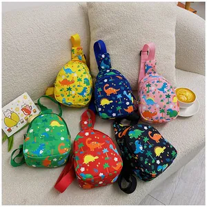 Bunte Kinder-Brusttaschen mit süßen Dino-Prints auf einem gemütlichen cremefarbenen Sofa.