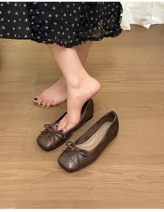 Close-up of brown square toe ballet flats with bow accent on a warm wood floor background