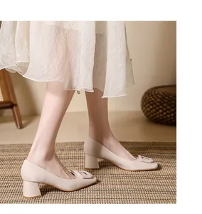 Elegant beige chunky heel pumps with square buckle detail shown on a textured rug