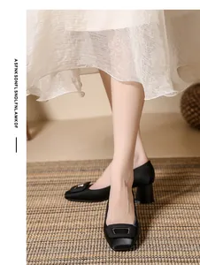 Detailed macro view of black satin chunky heel pumps featuring a stylish square buckle.