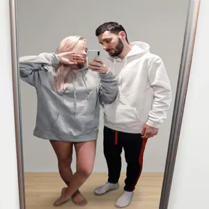Lifestyle shot of a couple wearing oversized grey and white hooded sweatshirts at home