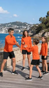 Family in matching orange long-sleeved athletic shirts playing outdoors by the sea