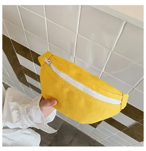 Main tenant un sac banane jaune vif en toile pour enfant sur un fond de carreaux blancs