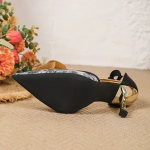 Detailansicht eleganter schwarzer spitzer Heels mit goldenem Stiletto und Dekoschleife.