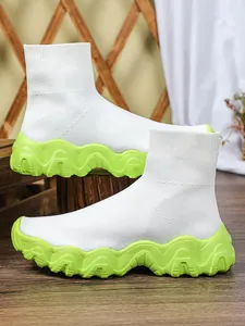 Detail van witte gebreide sok-sneakers met opvallende limoengroene golvende platformzolen.
