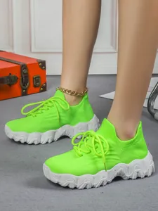 Detailansicht der neongrünen atmungsaktiven Fly-Knit-Sneaker für Damen mit dicken weißen Sohlen.