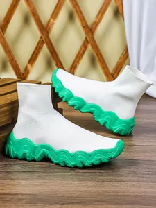 Detail van witte gebreide sok-schoenen met een opvallende groene golvende platformzool.