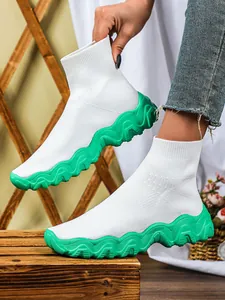 Detailweergave van witte fly-knit sok sneakers met opvallende groene golvende dikke zolen