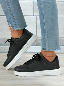 Dettaglio di eleganti sneakers nere con plateau e suola bianca indossate con jeans blu
