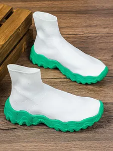 Detailweergave van witte gebreide sok-sneakers met dikke groene golvende rubberen zool