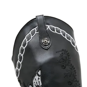 Close-up detail of white embroidery and floral metal stud on black leather Western boot