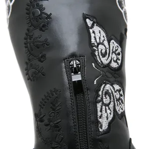 Detail shot of white butterfly embroidery and zipper on black leather western boots.