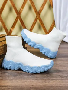 Detailopname van witte gebreide sok-sneakers met dikke lichtblauwe golvende zolen