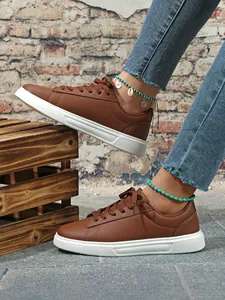 Dettaglio di sneaker marroni casual con spessa suola bianca e cavigliere di perline blu.