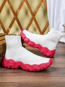 Dichtbij van witte gebreide sok-schoenen met dikke rode golvende zolen op hout