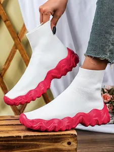 Zijaanzicht van witte gebreide sok-sneakers met golvende grove rode platformzolen