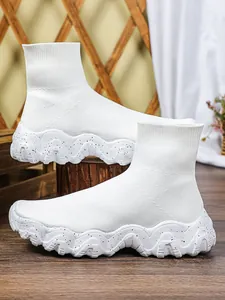 Gedetailleerd zijaanzicht van witte gebreide sok-sneakers met dikke golvende gespikkelde zolen.