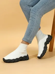 Close-up van witte ademende gebreide sok-sneakers met dikke zwarte gespikkelde zool