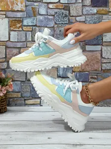 Detail view of stylish chunky multi-color platform sneakers on a rustic brick backdrop.