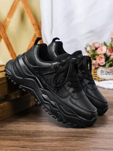 Detailed view of black chunky platform sneakers with thick wavy soles on a wooden floor.