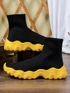 Detailopname van zwarte gebreide sok-sneakers met dikke gele golvende plateauzool
