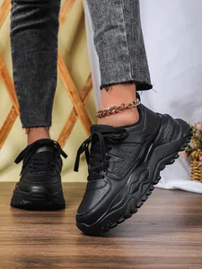 Close-up of black chunky sneakers featuring thick soles and a stylish gold anklet detail.
