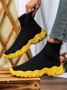 Detailopname van zwarte gebreide sok-sneakers met een dikke gele golvende zool