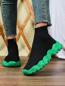 Detail van zwarte sok-sneakers met een opvallende groene dikke golvende zool sneaker