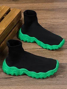 Detailweergave van zwarte fly-knit sok-sneakers met een dikke groene zool.