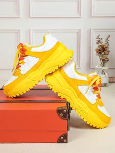 Vibrant yellow and white chunky dad sneakers displayed on a vintage red suitcase prop.