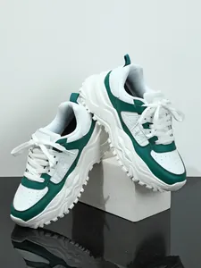 Modern white and green chunky sneakers displayed on a white block in a professional studio setting.