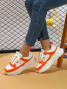 Close-up of trendy orange and white chunky platform sneakers worn with blue jeans