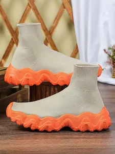 Gedetailleerde weergave van beige gebreide sneakers met dikke oranje gegolfde zolen.
