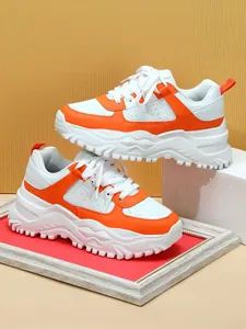 Detailed view of white and orange chunky sneakers with thick textured platform soles