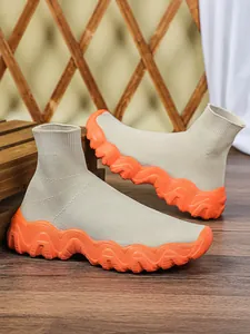 Detail van beige gebreide sok-sneakers met dikke, oranje gegolfde zool