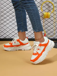 Detailed view of white and orange platform sneakers being worn by a person with jeans.