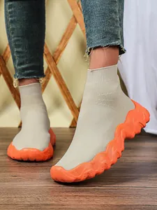 Detail van de dikke oranje gegolfde zool en beige gebreide textuur van de ademende sok sneaker.