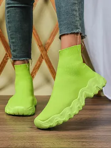 Close-up van limoengroene gebreide sok-sneakers met golvende platformzolen op model.