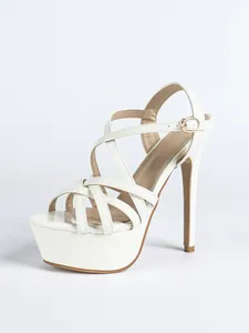 Detailed side view of white patent leather platform stiletto sandals with crisscross straps.