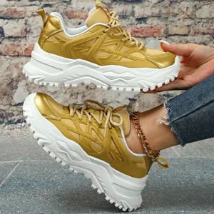 Close-up van trendy gouden chunky sneakers met dikke witte zolen en 'Running' detail.